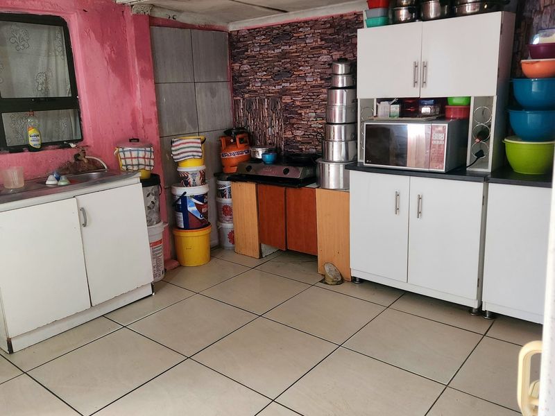 A functional kitchen space featuring tiled floors, built-in cabinetry, and a sink, currently requiring cosmetic updates and improved storage organization.