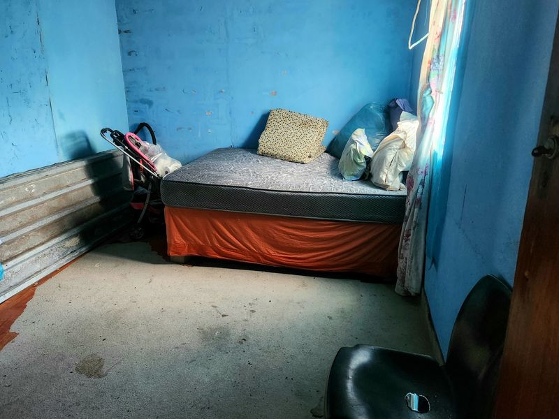 A small bedroom featuring blue painted walls with visible wear and corrugated metal wall paneling.