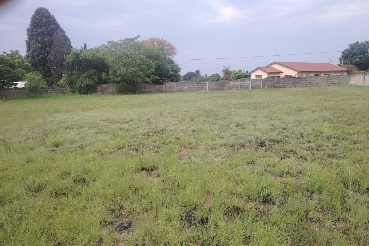 A vacant residential plot featuring a level grassed area enclosed by a precast concrete boundary wall and mature perimeter trees.
