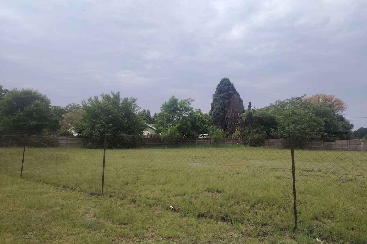 A view of a vacant residential plot featuring grass coverage and perimeter wire mesh fencing with a boundary wall in the background.