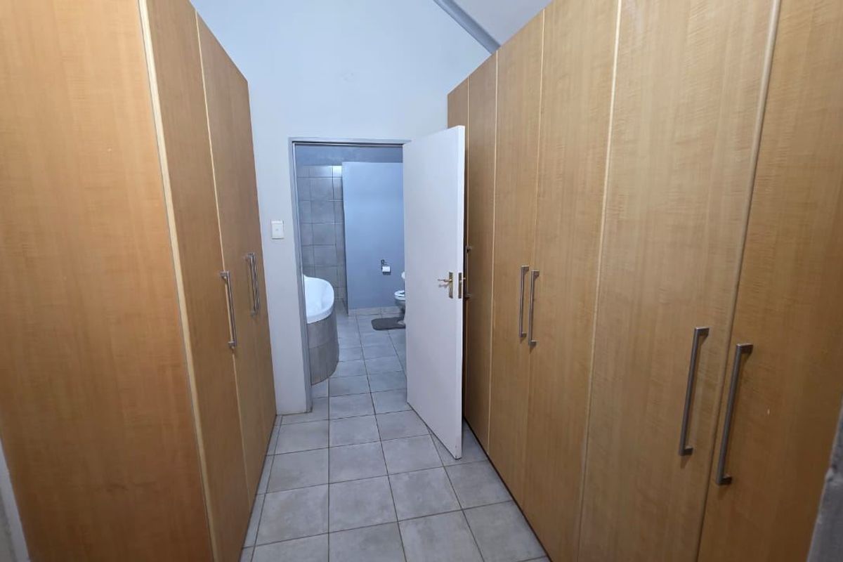 A bedroom dressing area featuring extensive built-in wooden cupboards and tiled flooring, leading directly into an en-suite bathroom.