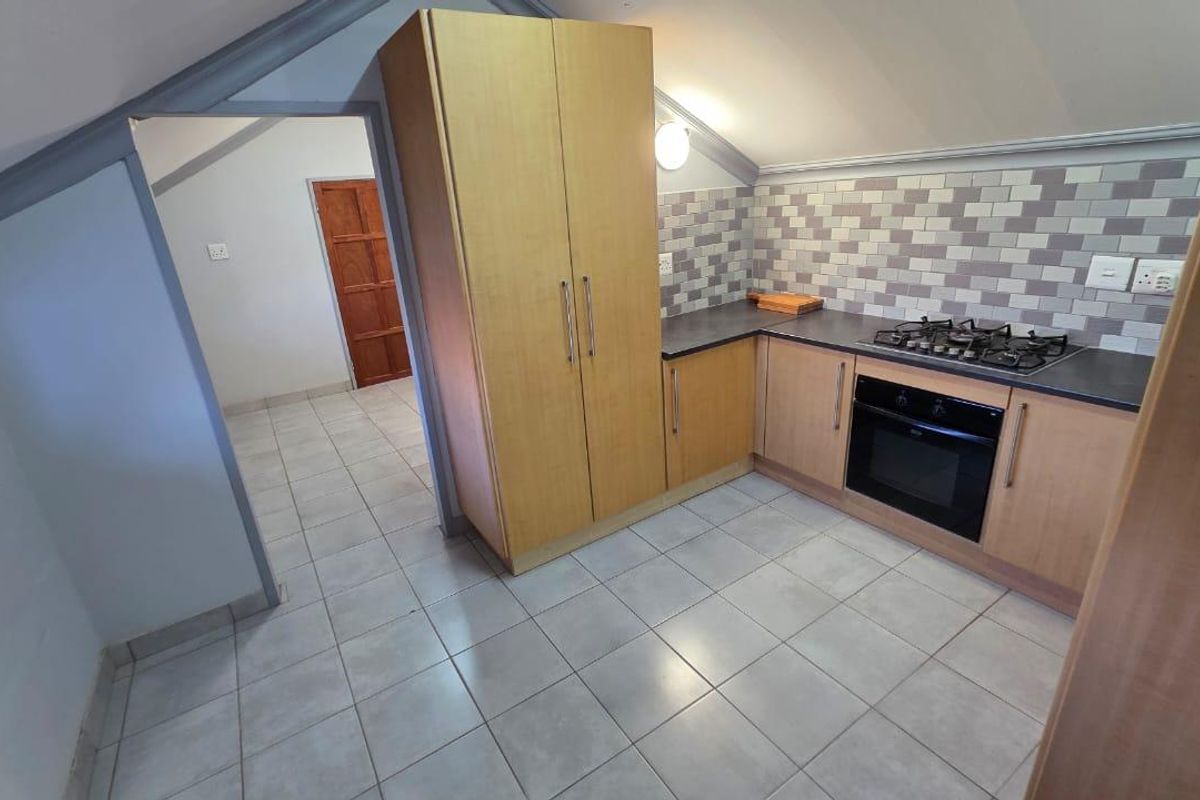 A compact kitchen featuring light wood cabinetry, a gas hob, built-in oven, and a tiled backsplash, situated under a sloped ceiling.