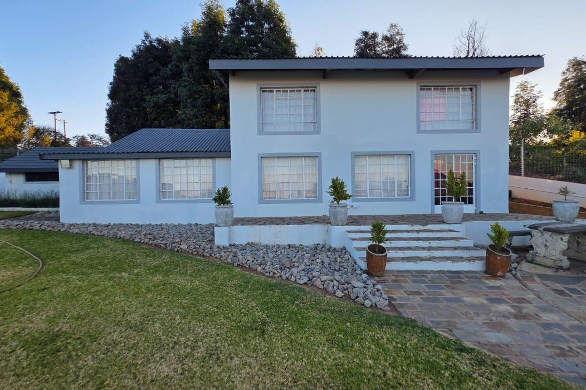A well-maintained two-story house exterior featuring a stone patio, concrete steps, and a spacious lawn area.