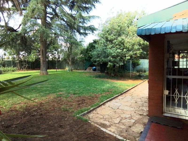 A spacious rear garden featuring a stone paved walkway, mature trees, and a brick exterior wall with a metal awning.