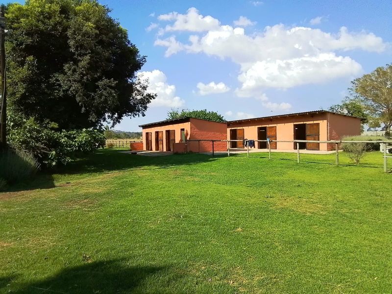 A view of the rear garden featuring a row of stable-style outbuildings with timber doors and surrounding green lawn space.