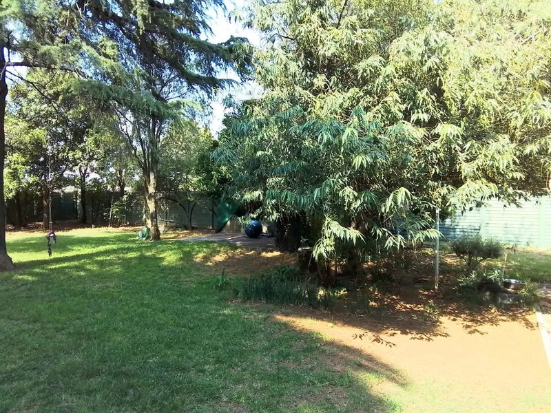 A spacious, established garden featuring mature trees, a well-maintained lawn, and perimeter fencing, providing a private outdoor setting.