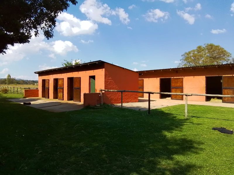 A row of stable blocks featuring individual timber doors, concrete apron, and post and rail fencing set within a grassy outdoor area.