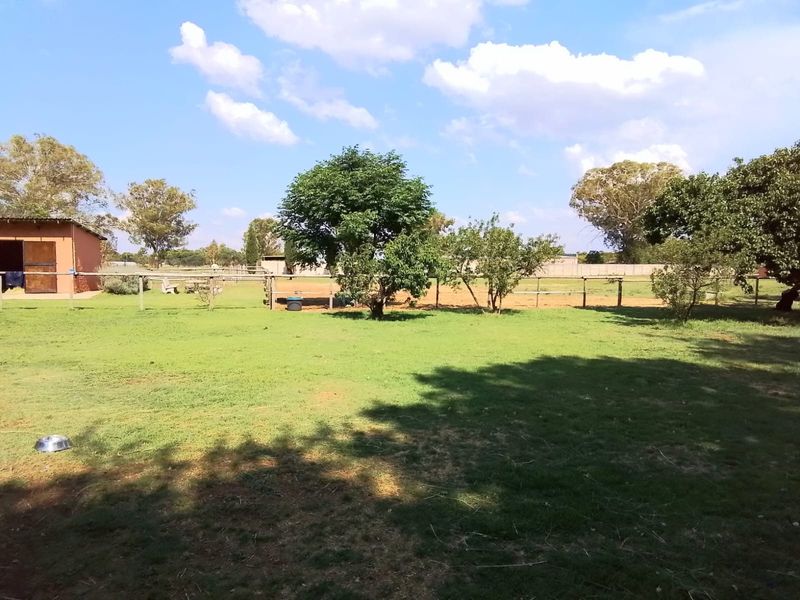Spacious garden area featuring a well-maintained lawn, mature trees, and post and rail fencing with an outbuilding in the background.