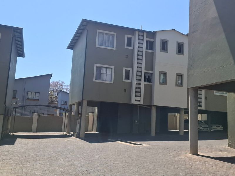 Exterior view of a modern apartment complex featuring elevated building structures, paved parking areas, and secure perimeter walling.