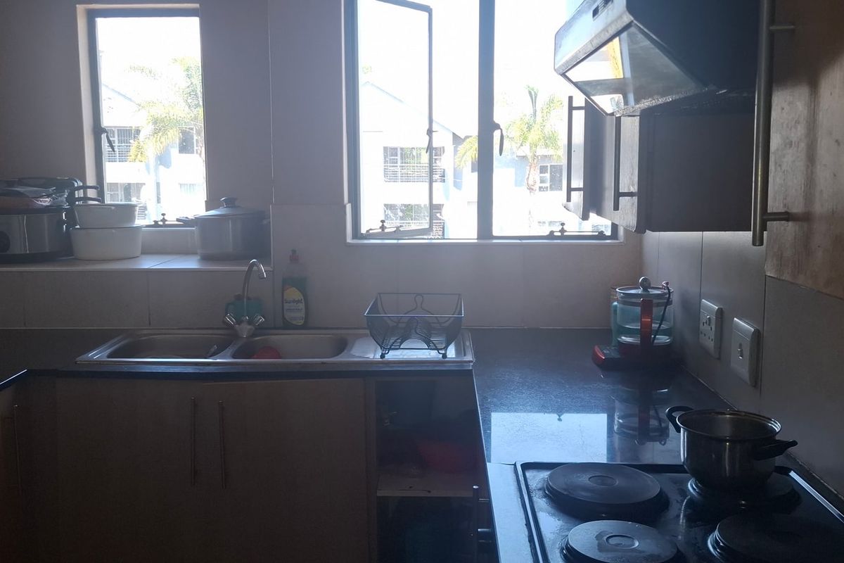 A functional kitchen featuring dark countertops, built-in cabinetry, a double sink, and an integrated electric hob with an extractor fan.