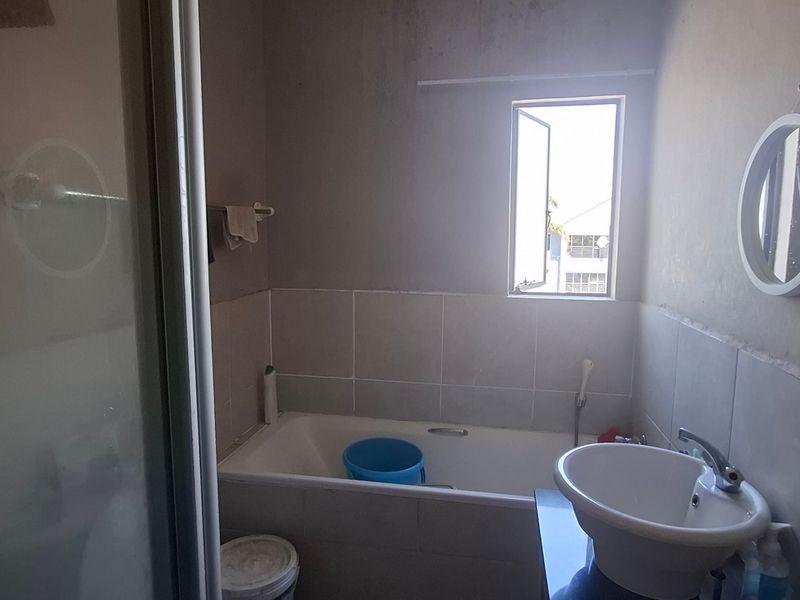 A compact bathroom featuring a bathtub with tiled surround, a pedestal basin, and a shower enclosure.