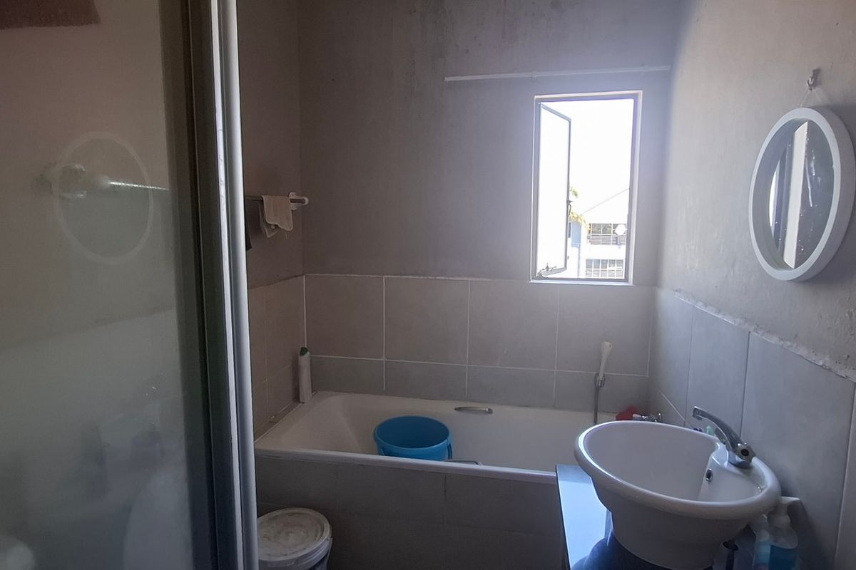 A compact bathroom featuring a bathtub with tiled surround, a pedestal basin, and a shower enclosure.