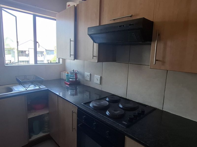 Functional kitchen featuring laminate cabinetry, dark granite countertops, a built-in electric hob, extractor fan, and a stainless steel sink with a window view.