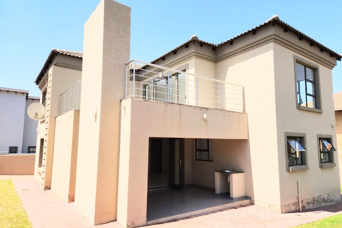 Rear view of the property featuring a covered patio with a built-in braai and an upper-level balcony with stainless steel balustrades.