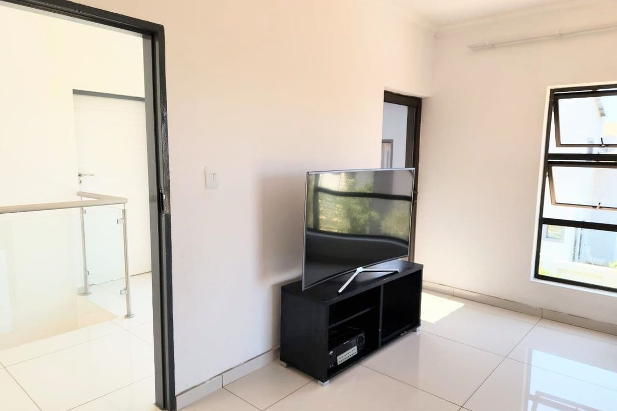 A bright living area featuring neutral tiled flooring, modern aluminium window frames, and clean white walls, providing a versatile space for relaxation.