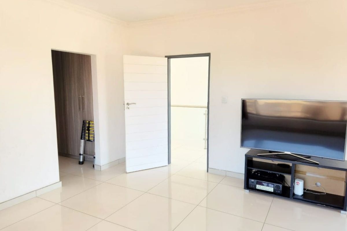 A bright bedroom featuring neutral tiled flooring, built-in cupboards, and a clean, minimalist aesthetic with direct access to an adjacent hallway.