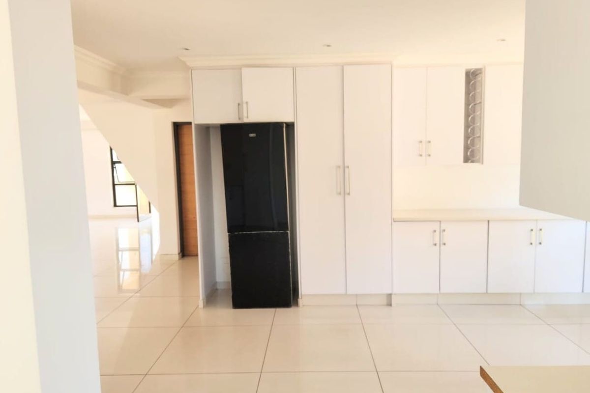 A bright, modern kitchen featuring white built-in cabinetry and clean tiled flooring, offering a spacious and neutral layout ready for personalization.