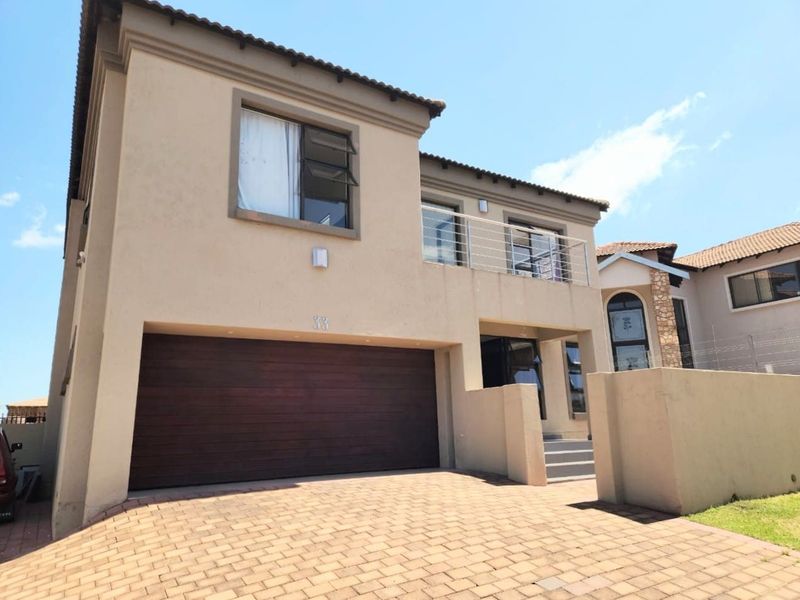 Front elevation of a two-story house featuring a paved driveway, integrated double garage, and an upper-level balcony with metal railings.