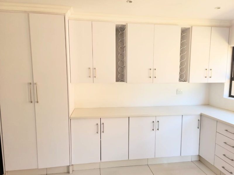 A clean, modern kitchen featuring white built-in cabinetry, ample counter space, integrated wine storage, and neutral tiled flooring.