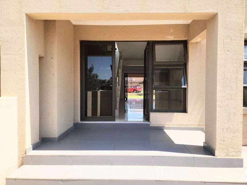 Covered front entrance porch with tiled flooring and modern aluminium door and window frames, providing a clear view through to the interior staircase.