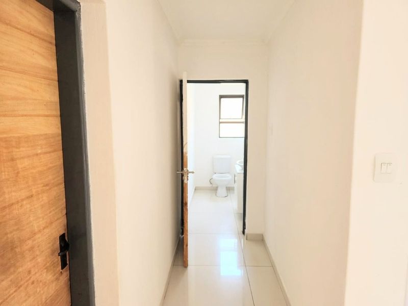 A clean, neutral hallway with tiled flooring leading towards a bathroom, featuring simple finishes and a bright, minimalist aesthetic.