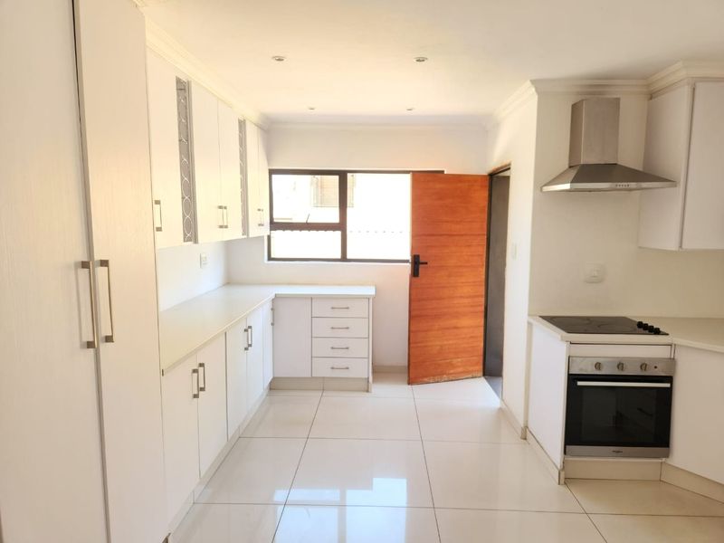 A clean, modern kitchen featuring white cabinetry, tiled flooring, and built-in appliances including an oven, hob, and extractor fan.