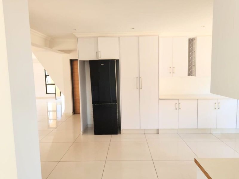 A bright, modern kitchen featuring white built-in cabinetry and clean tiled flooring, offering a spacious and neutral layout ready for personalization.