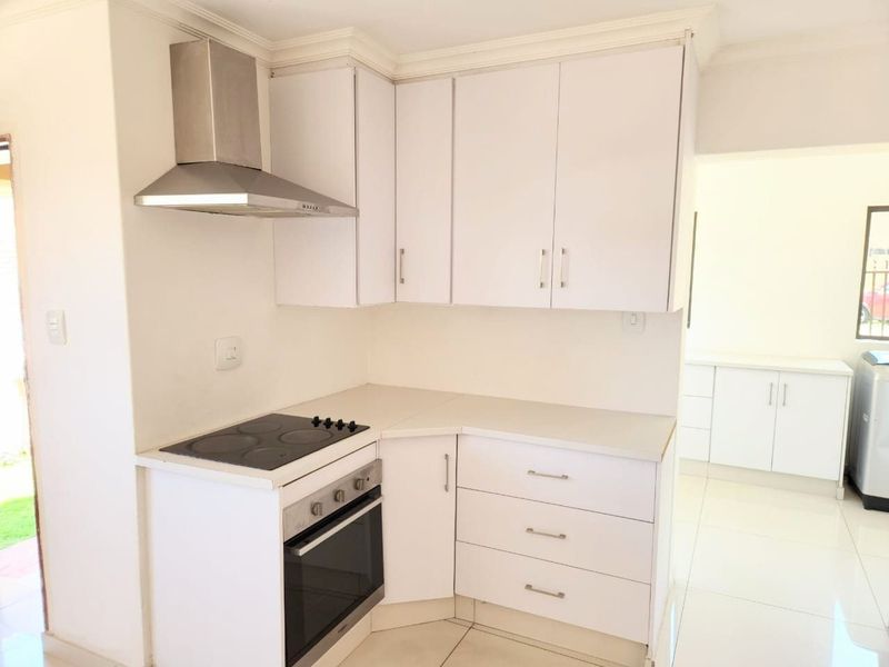 A clean, modern kitchen featuring white cabinetry, a built-in oven, electric hob, and stainless steel extractor fan with tiled flooring.