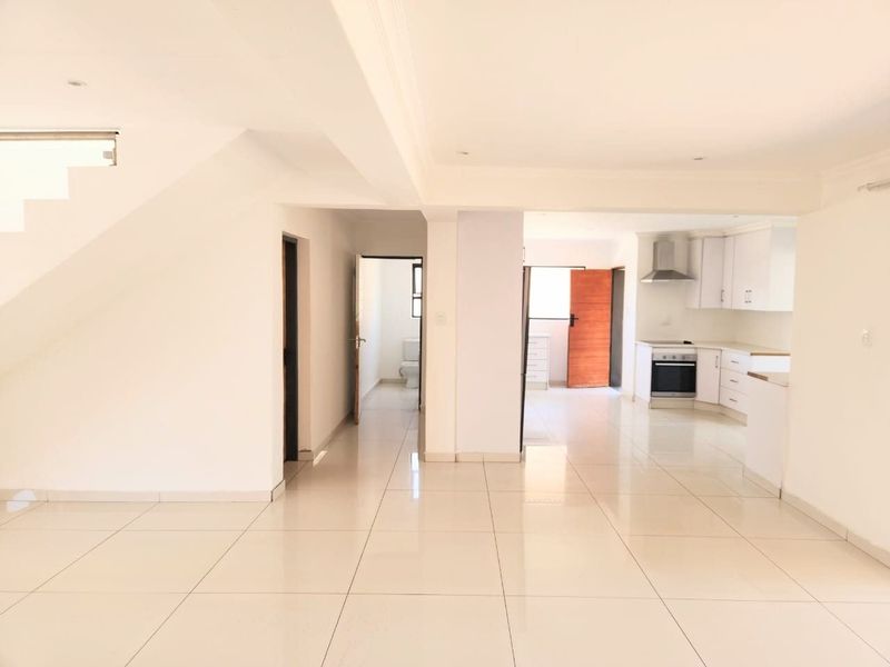 Spacious open-plan living area featuring tiled floors, a modern kitchen with built-in appliances, and a staircase leading to the upper level.