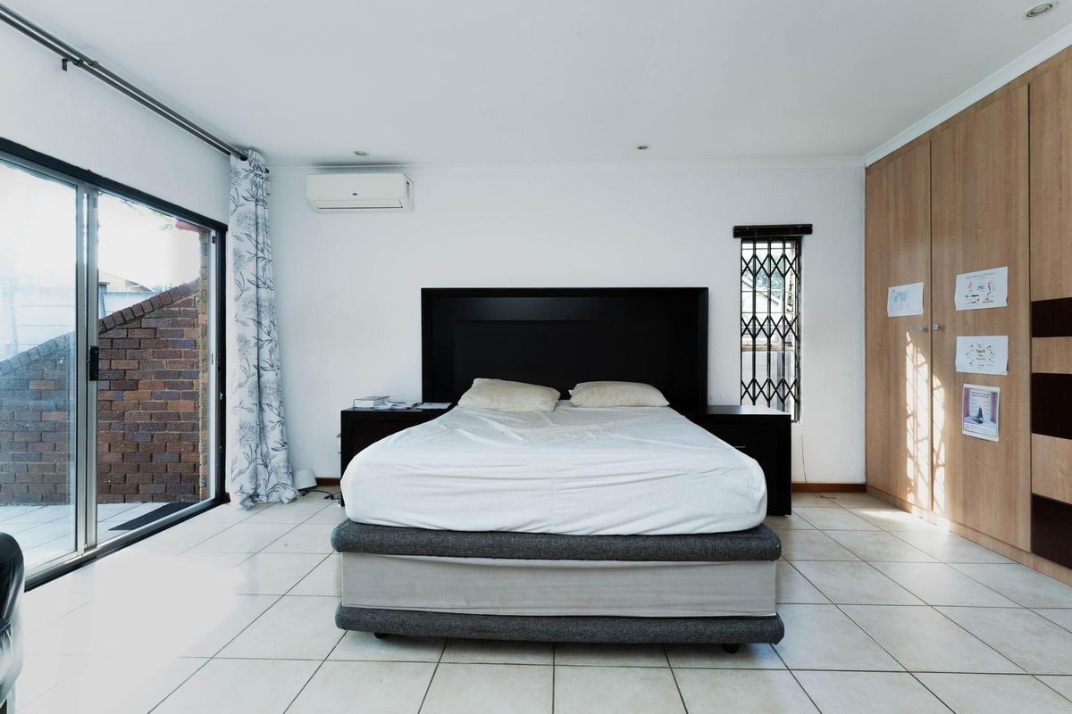Spacious bedroom featuring tiled flooring, built-in cupboards, a split-system air conditioner, and a sliding glass door providing access to the exterior.