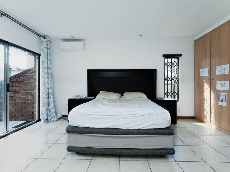 Spacious bedroom featuring tiled flooring, built-in cupboards, a split-system air conditioner, and a sliding glass door providing access to the exterior.
