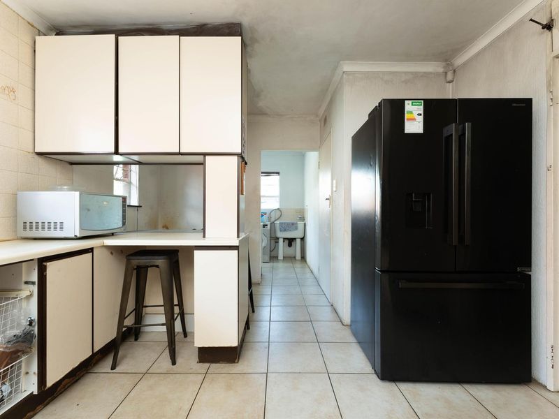 A dated kitchen featuring laminate cabinetry and tiled flooring, with a view through to a secondary utility or laundry area.