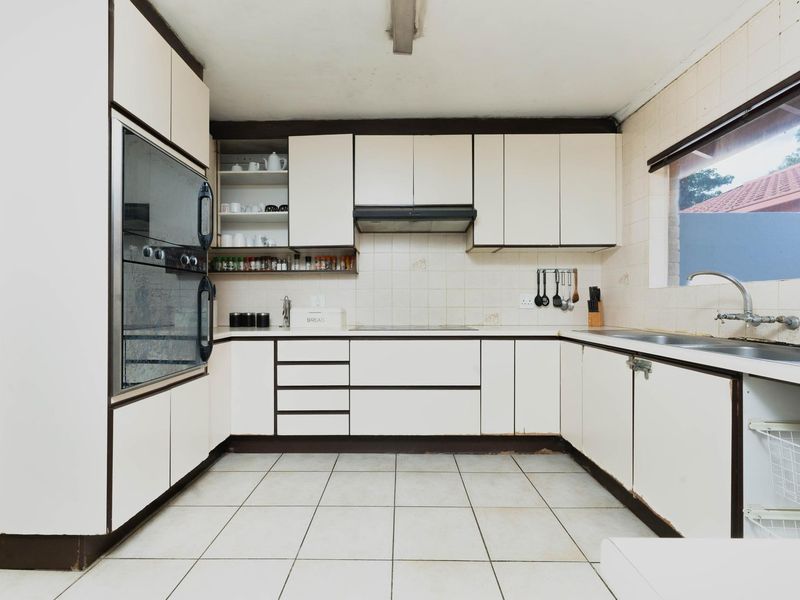A dated kitchen featuring built-in oven, extractor fan, ceramic hob, and double sink with tiled splashbacks and flooring.