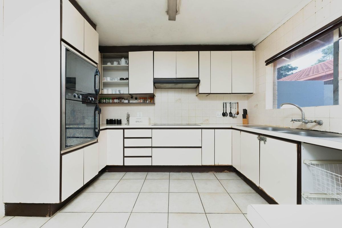 A dated kitchen featuring built-in oven, extractor fan, ceramic hob, and double sink with tiled splashbacks and flooring.
