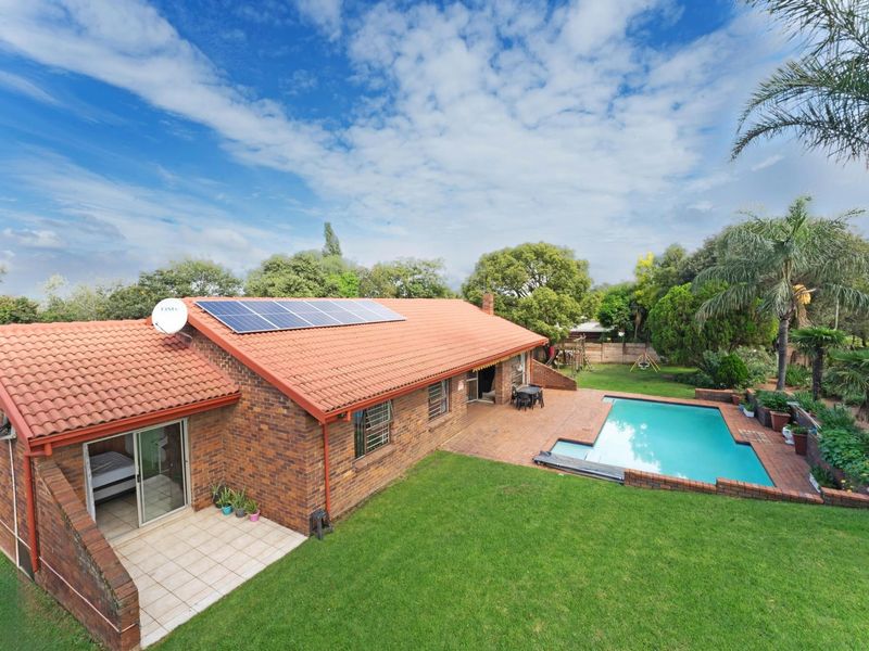 Rear view of a brick house featuring a swimming pool, paved patio area, and roof-mounted solar panels set within a landscaped garden.