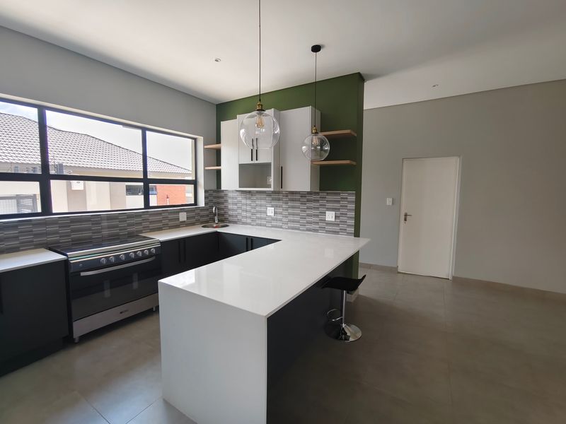 Modern kitchen featuring sleek quartz countertops, dark cabinetry, a built-in oven with gas hob, and stylish pendant lighting in an open-plan layout.