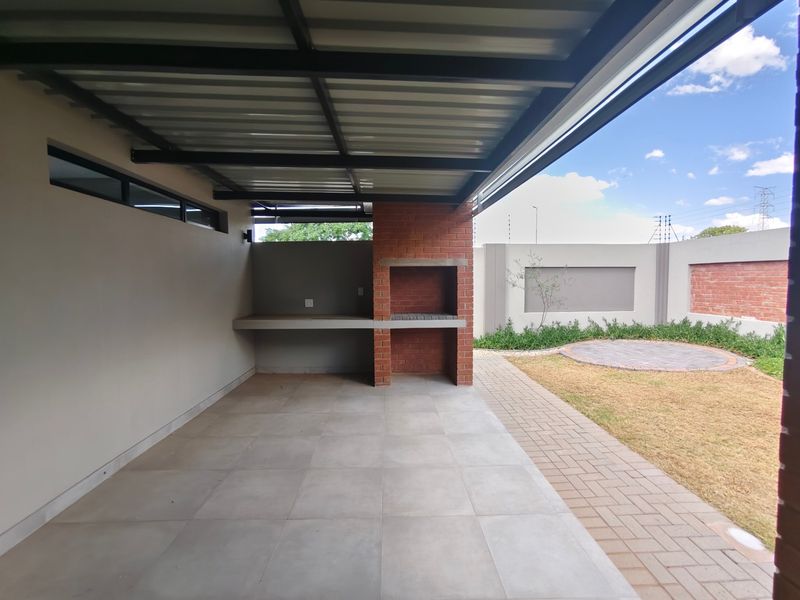 Covered patio area featuring a built-in brick braai, concrete prep counter, and direct access to a paved garden space.