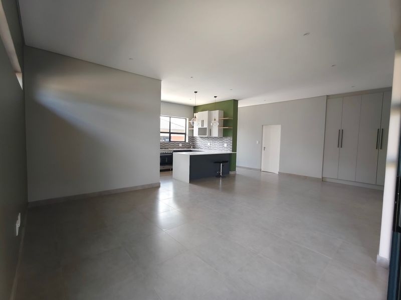 Spacious open-plan living area featuring a modern kitchen with a central island, sleek cabinetry, and neutral tiled flooring throughout.