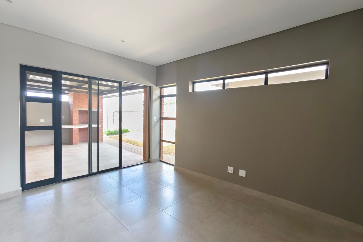 A bright, modern, and empty living area featuring large sliding glass doors that open onto a patio, with neutral tiled floors and clerestory windows.