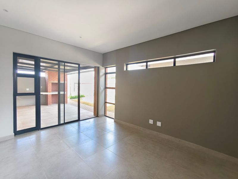 A bright, modern, and empty living area featuring large sliding glass doors that open onto a patio, with neutral tiled floors and clerestory windows.