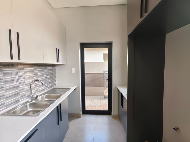 A modern, clean scullery featuring sleek two-tone cabinetry, a double stainless steel sink, and direct access to an outdoor paved area.