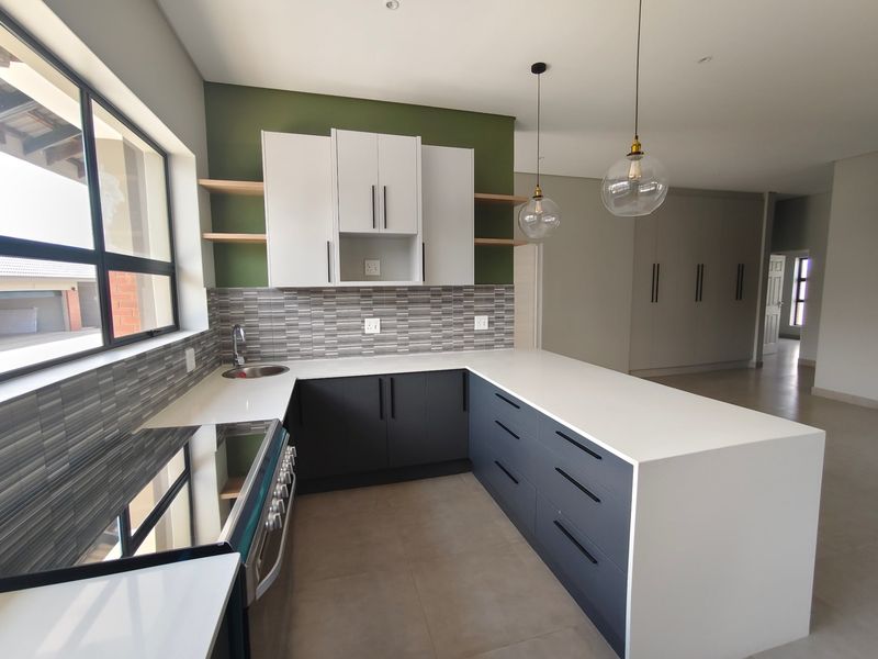 Modern kitchen featuring two-tone cabinetry, stone countertops, tiled backsplash, and a breakfast bar, complemented by contemporary pendant lighting and neutral floor tiles.