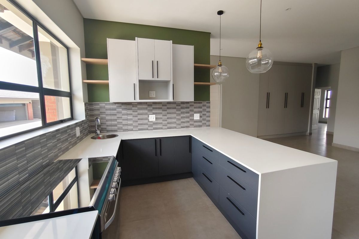 Modern kitchen featuring two-tone cabinetry, stone countertops, tiled backsplash, and a breakfast bar, complemented by contemporary pendant lighting and neutral floor tiles.