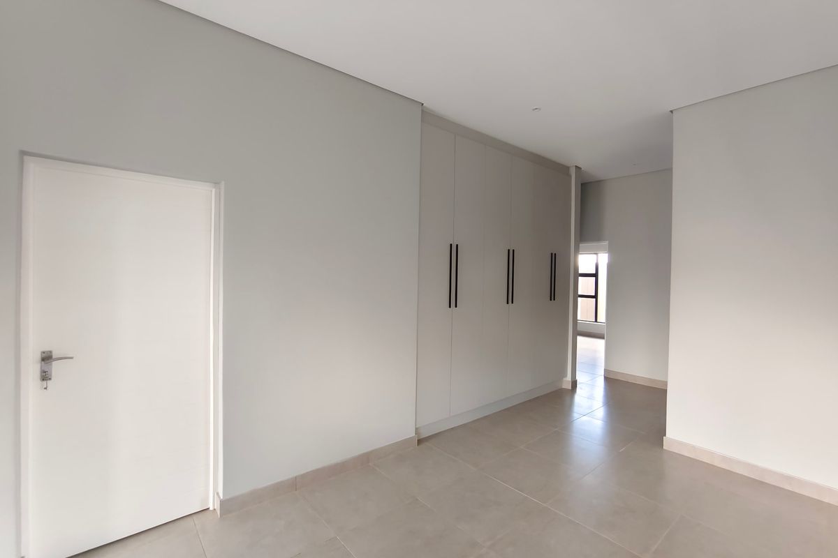 A bright, modern, and spacious bedroom featuring neutral tiled flooring and extensive built-in cupboard storage with sleek black handles.