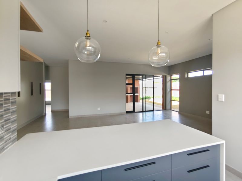 Modern open-plan living area featuring a sleek kitchen island with quartz countertops, pendant lighting, and seamless flow to an outdoor patio with built-in braai.