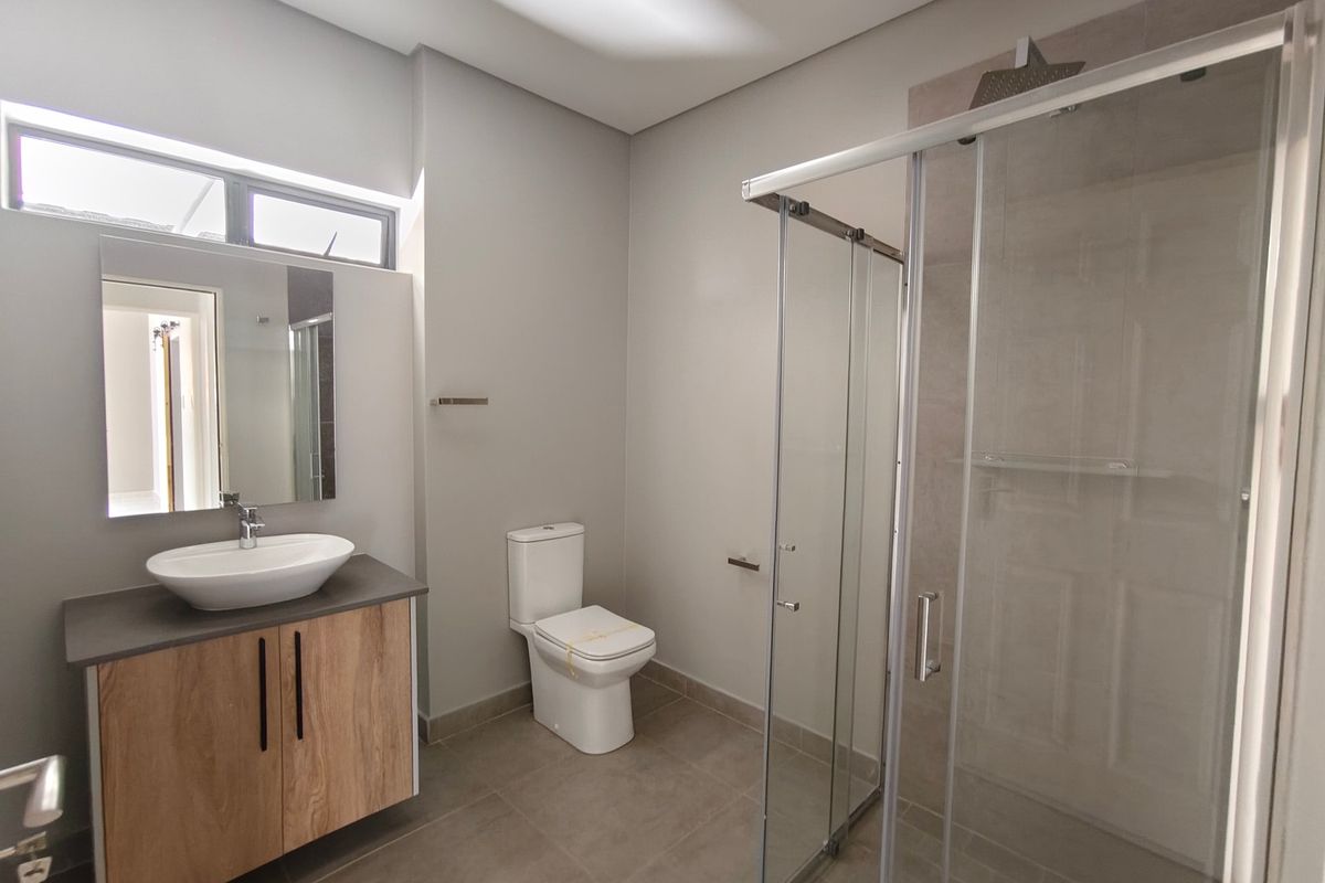 Modern bathroom featuring a wood-finish vanity with a vessel sink, a glass-enclosed shower, and neutral floor tiling.