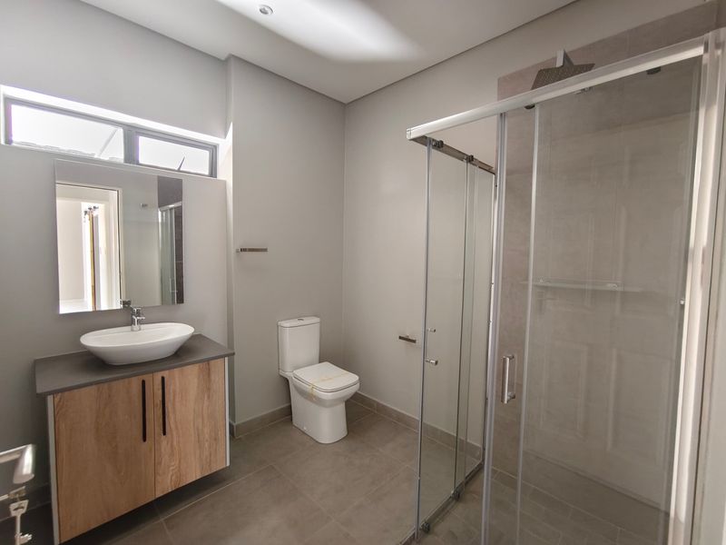 Modern bathroom featuring a wood-finish vanity with a vessel sink, a glass-enclosed shower, and neutral floor tiling.