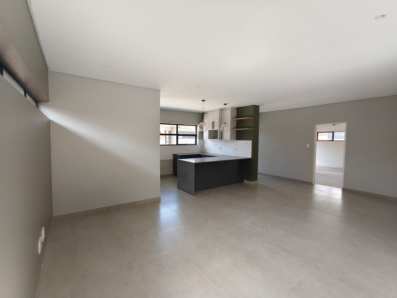 Spacious open-plan living and kitchen area featuring modern cabinetry, a central island, subway tile backsplash, and neutral tiled flooring throughout.