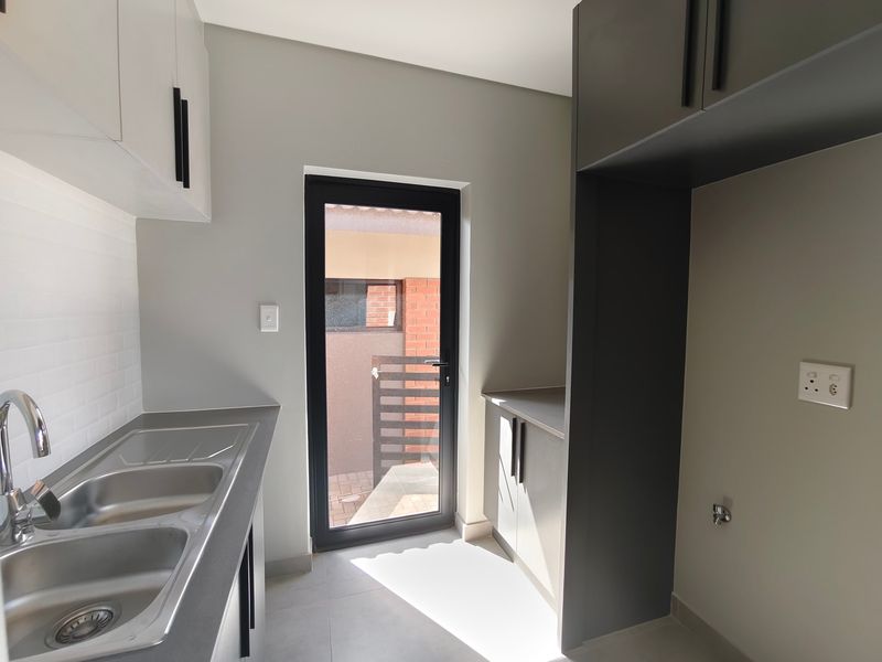 Modern scullery featuring sleek cabinetry, double bowl stainless steel sink, subway tile backsplash, and direct access to the exterior.