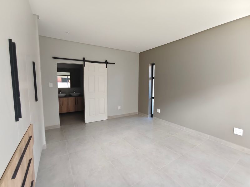 A modern, empty bedroom featuring neutral tones, tiled flooring, a sliding barn door, and an adjoining bathroom with dual vanity.